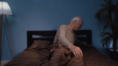 Yaşlı bir adam gece yatağa uzanıyor ve uyuyor. Erkek kişi battaniyenin altında yatıyor. Boşluğu kopyala