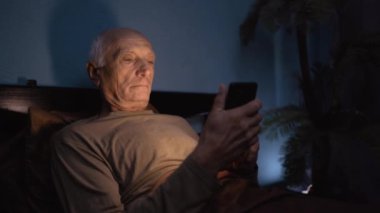 Yaşlı olgun bir adam gece yatağında akıllı telefon kullanır. uykusuzluk kavramı.
