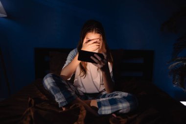 Gece yatağında cep telefonu kullanarak sosyal medya okuyan bir çocuk. Bağımlı bir genç. Uykusuzluk ve seyyar bağımlılık kavramı. Boşluğu kopyala