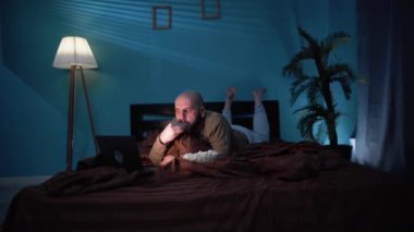 40 'lı yaşlarda sakallı bir adam yatakta yatarken patlamış mısır yiyor ve geceleri dizüstü bilgisayarda film izliyor. Boşluğu kopyala