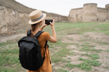 Sırt çantalı kadın fotoğrafçı eski antik kalenin fotoğrafını çekiyor. Seyahat ve hobi kavramı