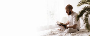 Kızıl sakallı adam kitap okuyor. Sabahları yatak odasında kitap okuyor. Boş zamanların ve hafta sonlarının tadını çıkarıyor. Pankart. Boşluğu kopyala