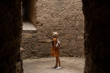 Kadın turist, antik bir kalenin tuğla duvarlarıyla kuleye bakıyor. Boşluğu kopyala