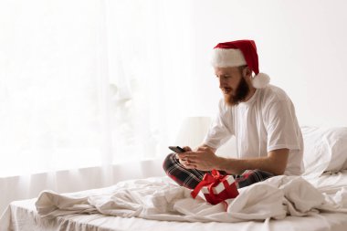 Noel Baba şapkalı sakallı adam akıllı telefon kullanıyor ve Noel sabahı alışveriş yapıyor. Boşluğu kopyala