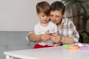 Orta yaşlı bir anne genç oğluna plastikten figürler yapmayı ya da hamur oynamayı öğretir. Boşluğu kopyala