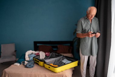 Son sınıf öğrencisi sarı bavulunu hazırlayıp telefonuna mesaj atıyor rahat bir evde seyahat beklentisine hazırlanıyor. Rezervasyon uygulaması kullanıyor. Boşluğu kopyala