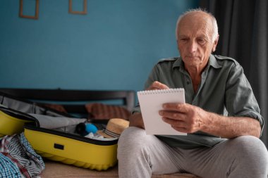 Seyahat için toplanacak eşyaların listesini yapıyorum. Kağıt yazan kıdemli adam bavulunu ve bavulunu tatile götür, elbiselerini bagaja koy. Seyahat tatili kavramı