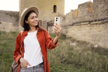 Şapkalı Latin Amerikalı kadın turist gün batımında antik kalede selfie çekiyor. Boşluğu kopyala