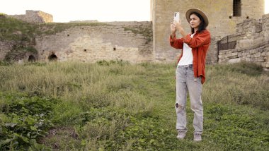 Bir seyahat blogu için antik bir kalenin fotoğraflarını çeken bir kadın turist. Tarihi yerleri belgelemekten ve seyahat deneyimlerini online olarak paylaşmaktan, kültür ve mimariyi araştırmaktan hoşlanıyor..