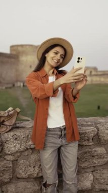 Gezisi sırasında kameraya bakarken eski kalenin önünde selfie çeken mutlu kadın gezgin. Boşluğu kopyala