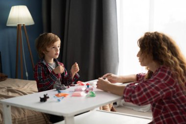 Anne ve küçük oğlu oyuncak çamurdan eğlenceli şekiller yaratırken aynı zamanda rahat bir evde oturup, el yapımı figürler ve aile aktivitelerine odaklanıyorlar. Boşluğu kopyala