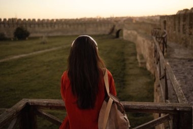 Kulaklıkla müzik dinleyerek antik kaleyi gezen kadın turistin arka görüntüsü. Turizm ve seyahat kavramı