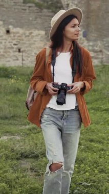Şapkalı güzel bir kadın turist elinde bir kamerayla eski bir kalenin içinden geçiyor ve güzel manzaraların resimlerini çekiyor..