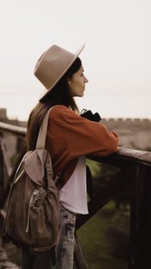 Elinde kamerayla gezen turist kadın, gün batımında nefes kesen antik bir kalenin manzarasının tadını çıkarıyor. Anın güzelliğine ve dinginliğine dalmış bir şekilde. dikey video