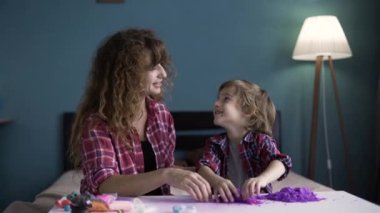 Beyaz bir anne, küçük oğlu bebeğe sarılırken kinetik kumla oynuyor. Oyun, eğlence ve annelerin sevgisi.