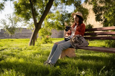 Şapkalı İspanyol turist kadın parktaki bankta güneşli havanın tadını çıkarıyor. Konsept rahatlama, seyahat ve doğa