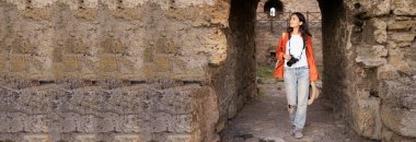 Kameralı bir kadın gezgin antik bir kalenin taş girişinden geçiyor. Gezmekten, anları yakalamaktan ve yolculuğundaki tarihi yerleri keşfetmekten hoşlanır.