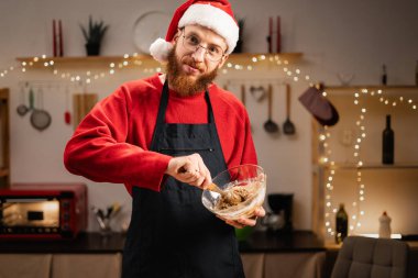 Noel Baba şapkalı sakallı bir adamın portresi Noel kurabiyesi yaparken mutfakta zencefilli kurabiye yapıyor, Noel tatillerinde mutlu kadın yemekleri yapıyor. Boşluğu kopyala
