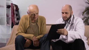 Üst düzey bir adam, ev ziyareti sırasında ona tıbbi raporları gösteren bir doktorla konuşuyor. Boşluğu kopyala