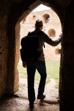Emekli erkek turist, uzayın yakınında duran antik bir kalenin tuğla duvarlarının içinden yazı için kemerden bakıyor. seyahat ve turizm kavramı