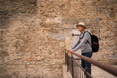 Yaşlı gezgin kalenin balkonunda durup, düşünceli bir şekilde tarihi mimariye bakıyor. Bir şapka ve sırt çantası takarak, korkuluklara yaslanır, yolculuğu boyunca antik duvarların manzarasının tadını çıkarır..
