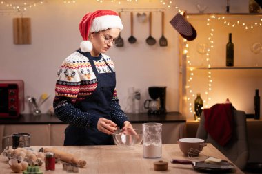 Önlüklü kadın Noel için kurabiye yapıyor mutfakta yemek yapıyor şeffaf kaseye yumurta kırıyor, mutlu noeller ve mutlu yeni yıl konsepti.
