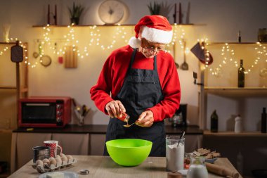 Yılbaşı mutfağında Noel Baba şapkası takan yaşlı adam Noel kurabiyeleri için hamur hazırlıyor. Boşluğu kopyala