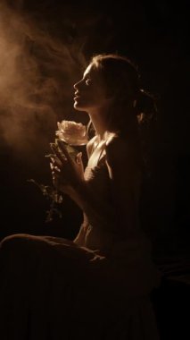 Gül çiçekli güzel bir kızın silueti, koyu duman arka planında rüya gibi bir genç kadının yüzü, güzellik ve basitlik kavramı. Boşluğu kopyala