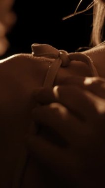 Elbise askısını nazikçe ayarlayan, yumuşak, sıcak ışıkta yakalanmış bir kadının yakın çekimi. Görüntü zarafet duygusunu, inceliği, kadınsı ayrıntıları ve hassas hareketleri çağrıştırır..