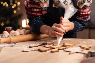 Noel kurabiyelerini ahşap masada kremayla süsleyen bir kadın. Fırında pişmiş noel kurabiyelerini süslüyordum. Yakın plan.
