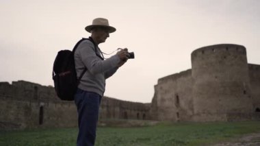 Sırt çantalı, tarihi yerleri fotoğraflayan emekli bir erkek turist akşam saatlerinde antik kalenin resimlerini çekiyor. Konsept seyahat, keşif ve tarihsel mimari fotoğrafçılık