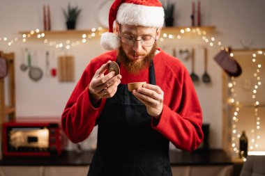 Genç adam mutfakta yemek pişiriyor ve pişirmek için baharat seçiyor. Noel atmosferinin hoş kokusunun tadını çıkarıyor. Boşluğu kopyala