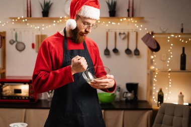 Noel Baba şapkalı bir adam mutfakta kurabiye hamuru karıştırıyor. Boşluğu kopyala