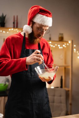 Noel şapkalı bir adam evdeki mutfağında Noel kurabiyesi pişiriyor. Boşluğu kopyala