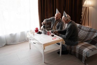 Milenyum çocuğu ve yaşlı babası doğum gününü evde kanepede oturup pasta yiyerek kutluyorlar. Aile kutlama konsepti