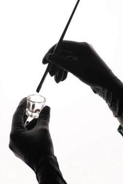 Siyah eldivenli bir güzellik uzmanının ellerinde bir fırça ve beyaz arka planda renkleri olan küçük bir cam kap var. Kaş tedavisinde tek renkli estetik vurgu hassasiyeti.