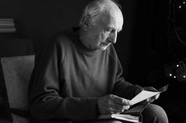 Elinde retro fotoğraflarla albüm tutan yaşlı bir adam, Noel arifesindeki çocuğunu hatırlıyor. Mutlu anılar ve nostalji konsepti. Siyah beyaz fotoğraf