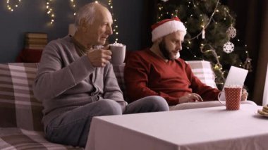 Emekli adam ve yetişkin oğul kanepeye oturmuş serbest çalışan genç adam evde Noel 'de çay içen yaşlı adamı kullanıyor. Boşluğu kopyala