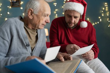 Milenyum adamı ve yaşlı babası Noel arifesinde evdeki koltukta oturan aile fotoğraflarına bakıyor. Boşluğu kopyala