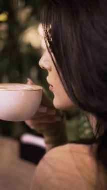 Kapuçino ya da latteden kadınların dudaklarında köpük kahve içen bir kızın yakın çekimi. Sabah kahve konsepti. Dikey video