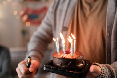 Yıl dönümü ya da doğum günü pastası ve mum tutan adamın ellerini yakın. Kırpılmış görünüm