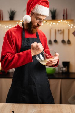 Noel Baba şapkalı sakallı adam evdeki rahat mutfakta Noel kurabiyesi pişiriyor. Boşluğu kopyala