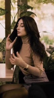 Kafe masasında tek başına oturan esmer, genç bir kadın gözlerini kaçırıp arkadaşlarını bekliyor. Dikey video