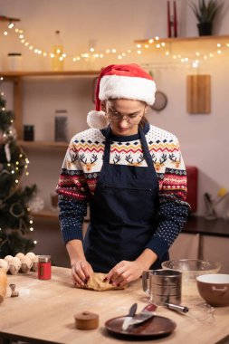 Noel için zencefilli kurabiye yapma süreci. Noel Baba şapkalı bir kadın mutfaktaki bir masaya hamur yoğurur ve hamur işi hazırlar. Boşluğu kopyala