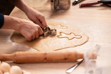 Dişi eller çiğ hamurdan şekiller keser ve Noel kurabiyeleri yapar. Yakın plan.