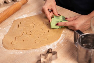 Noel kurabiyesi pişirmek. Dişi ellerin yakın çekimi, ahşap arka planda üst görünüm, kesicilerle zencefilli kurabiye yapmak. Boşluğu kopyala