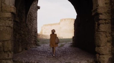 Eski kalenin içinde taş yolda yürüyen ve eski şehirleri gezen, elbise giymiş genç kadın turistin arka görüntüsü. Boşluğu kopyala