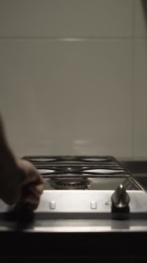 Eldiven giymiş kadın eller, tavaya paslanmaz tava koyuyor, gaz sobasında pişiriyor. Yakın plan. Dikey video
