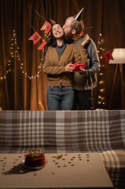Erkek hediye verir ve doğum günü partisinde kadınını öper. Çift evde, oturma odasında doğum gününü kutlar. Boşluğu kopyala