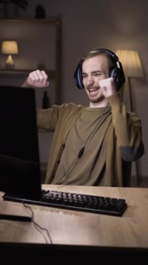 Beyaz tenli genç sporcu oyuncu geceleri evdeki bilgisayarda çevrimiçi video oyunu oynuyor. Oyuncu oyun sırasında keyifli anlar yaşıyor. Masada dans etmek..